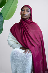 Woman wearing a red hijab and white outfit against a light background