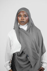 Woman wearing a gray hijab and white shirt on a plain background