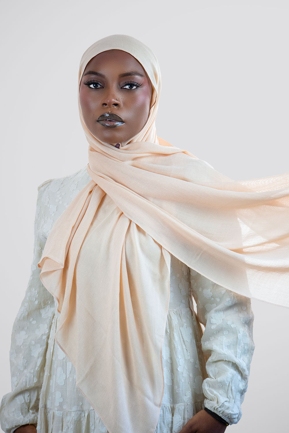 Woman wearing a beige hijab and light-colored top against a white background