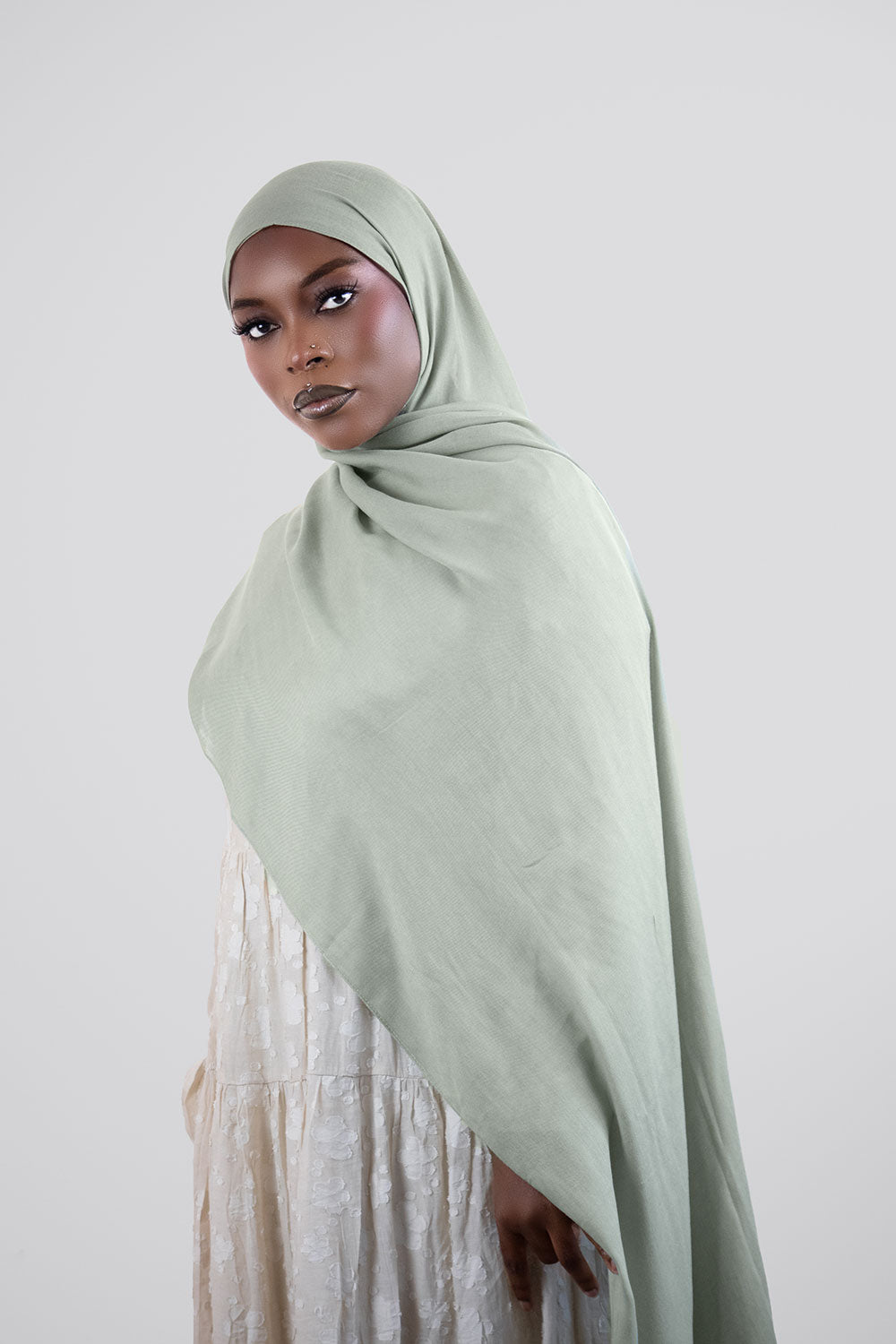 Woman wearing a light light olive hijab against a white background