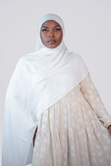 Woman wearing a white hijab and beige dress against a plain background