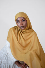 Woman wearing a mustard hijab against a plain background
