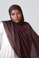 Woman wearing a brown hijab against a plain background