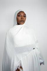 Person wearing a white hijab and dress against a plain background
